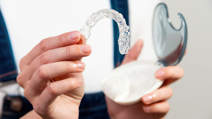Clear dental aligner held above its case, showcasing a removable orthodontic solution for teeth straightening at iLUMNA Dental in Jayanagar.